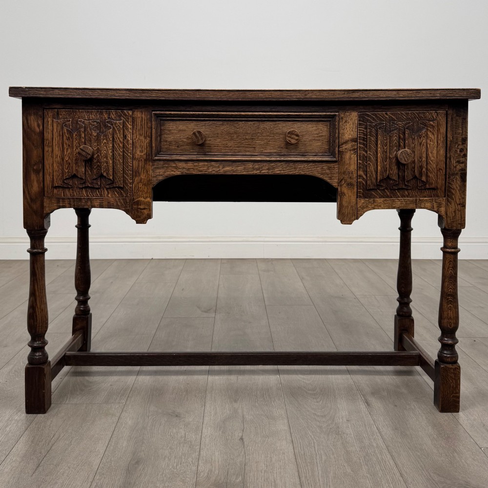 An Edwardian oak writing desk featuring three drawers with geometric carved fronts, turned legs, and a lower stretcher base.