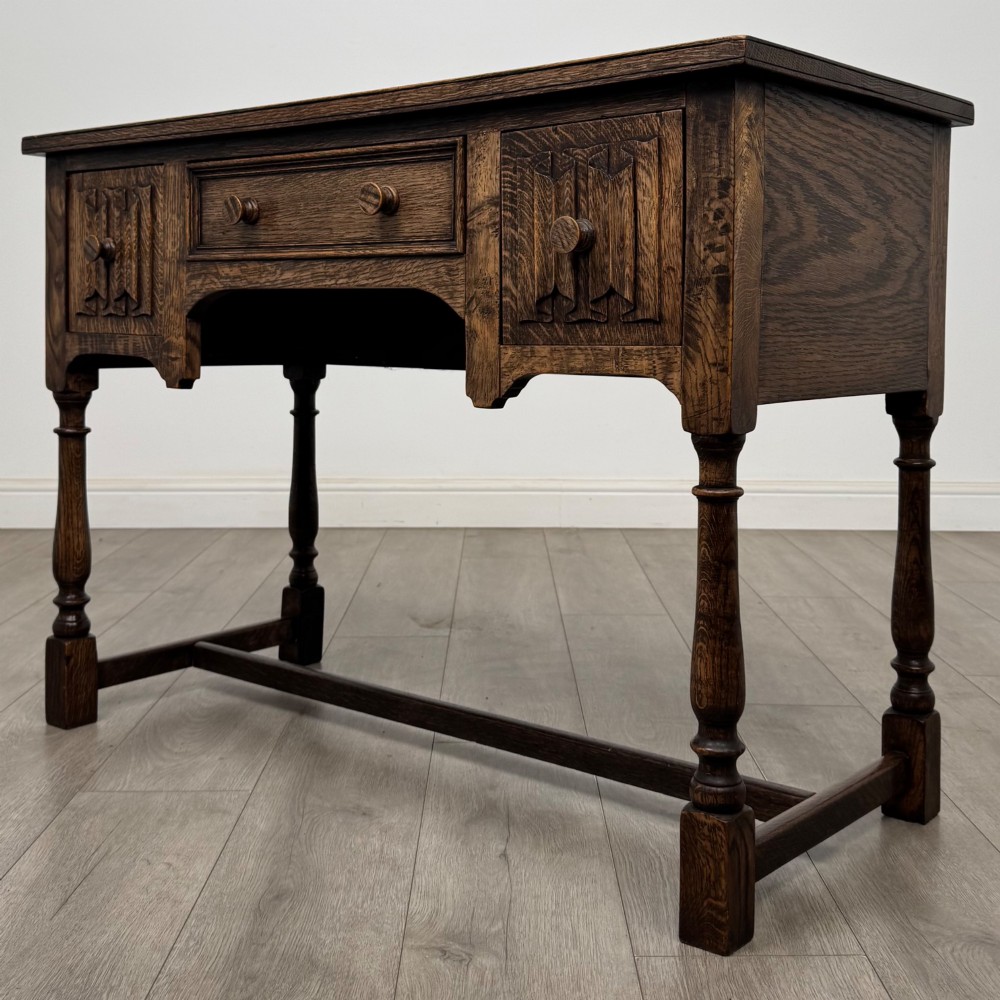 An Edwardian oak writing desk featuring three drawers with geometric carved fronts, turned legs, and a lower stretcher base. View II