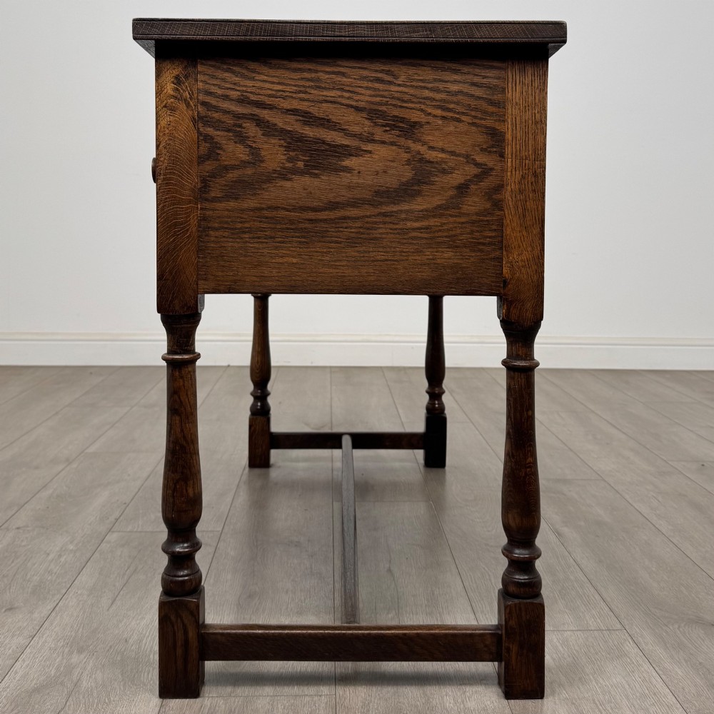 An Edwardian oak writing desk featuring three drawers with geometric carved fronts, turned legs, and a lower stretcher base. View III