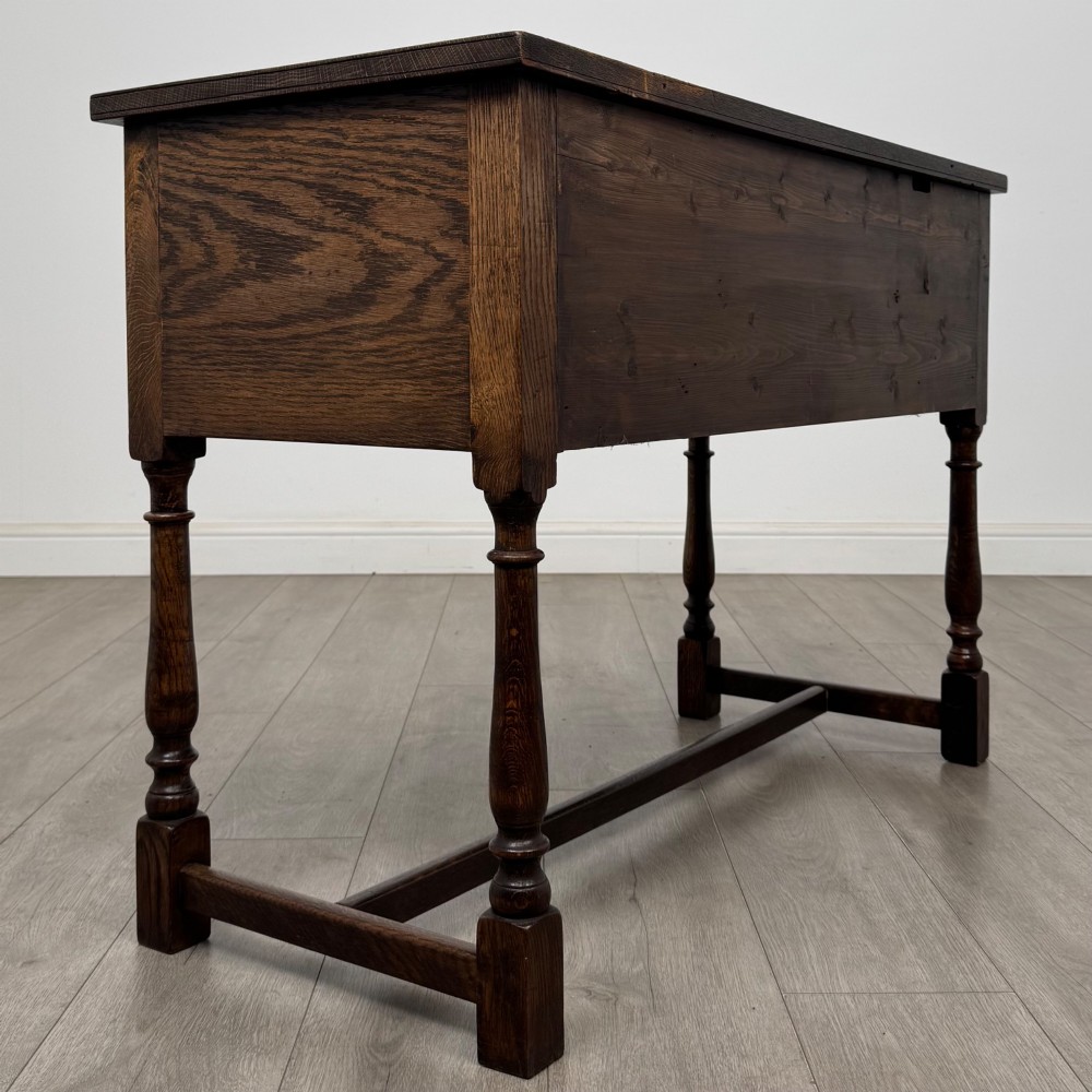 An Edwardian oak writing desk featuring three drawers with geometric carved fronts, turned legs, and a lower stretcher base. View IV