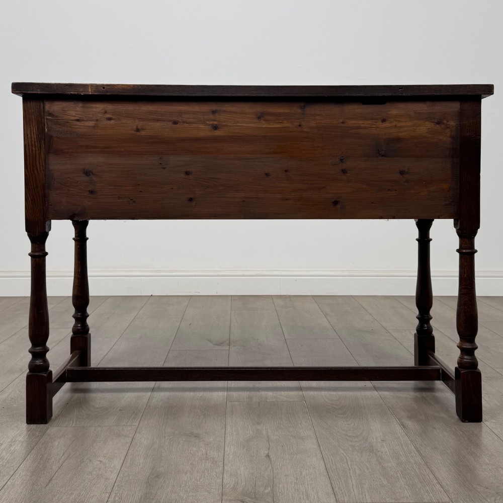 An Edwardian oak writing desk featuring three drawers with geometric carved fronts, turned legs, and a lower stretcher base. View V