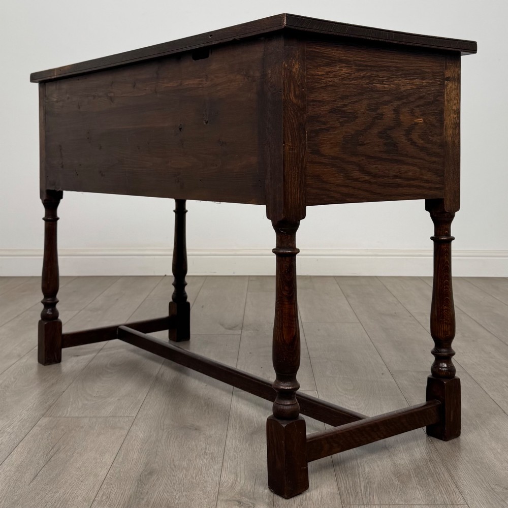 An Edwardian oak writing desk featuring three drawers with geometric carved fronts, turned legs, and a lower stretcher base. View VI