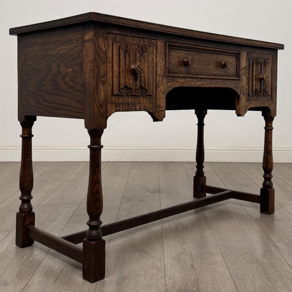 An Edwardian oak writing desk featuring three drawers with geometric carved fronts, turned legs, and a lower stretcher base. View VIII