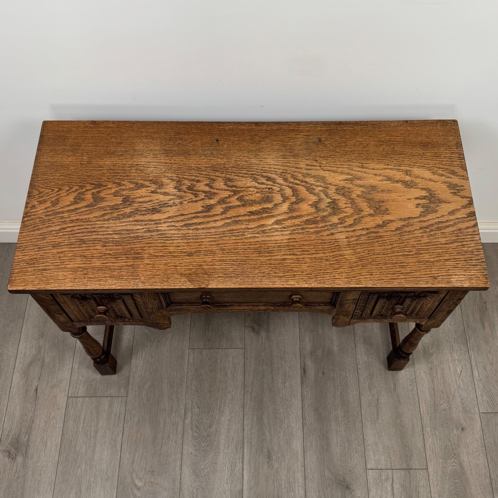 An Edwardian oak writing desk featuring three drawers with geometric carved fronts, turned legs, and a lower stretcher base. View IX