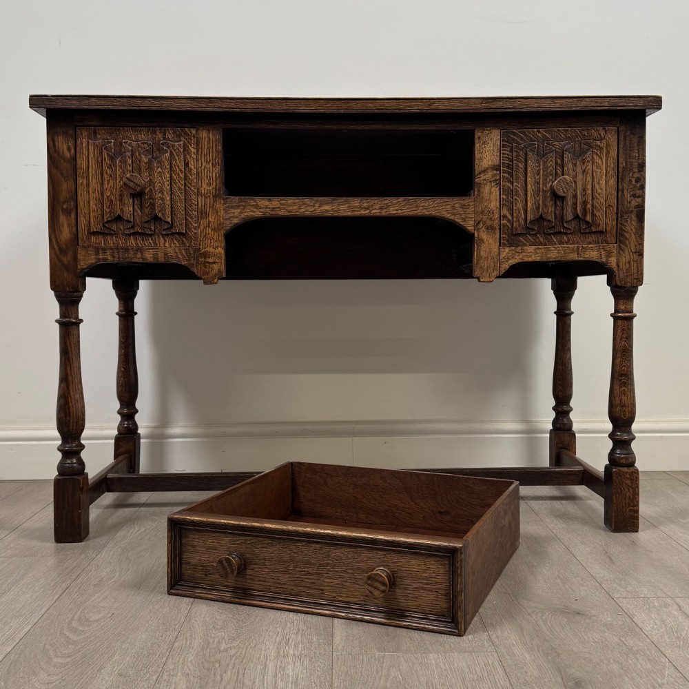 An Edwardian oak writing desk featuring three drawers with geometric carved fronts, turned legs, and a lower stretcher base. View X