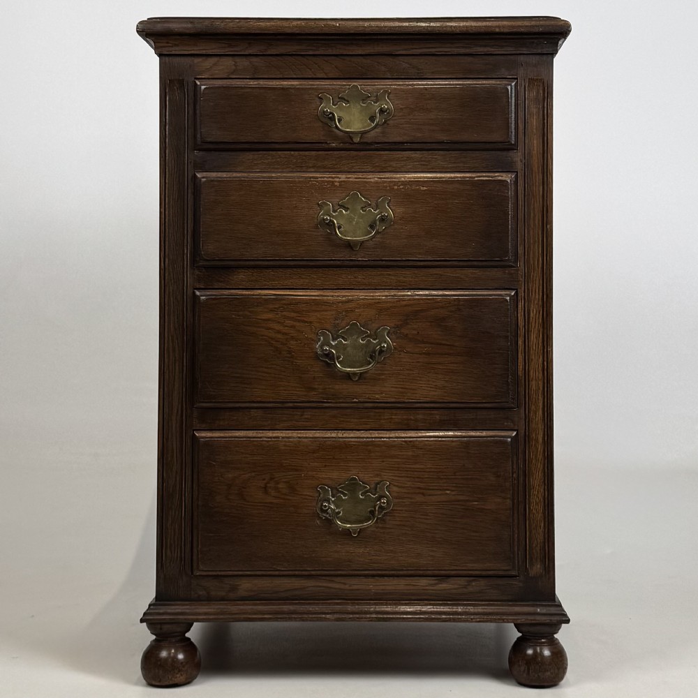 A small dark oak Edwardian chest featuring four drawers with brass drop handles and turned bun feet.