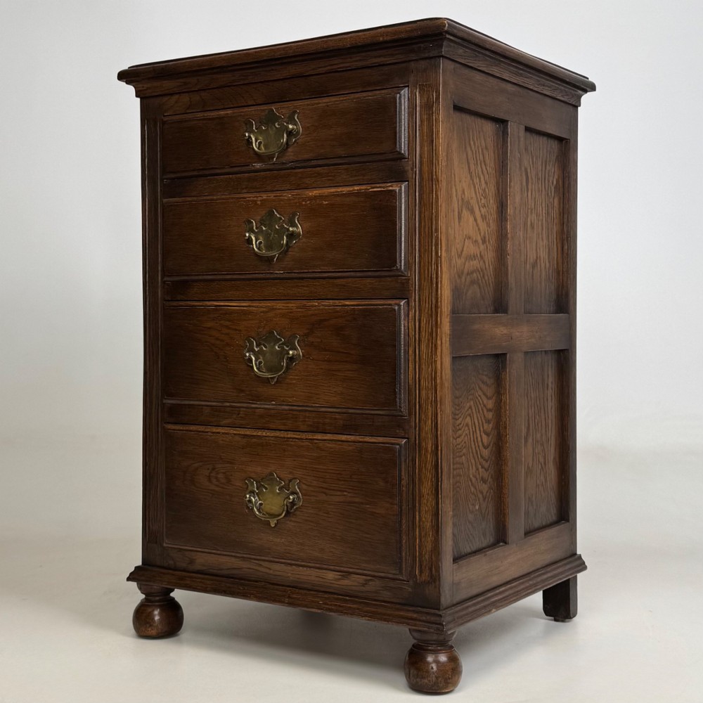 A small dark oak Edwardian chest featuring four drawers with brass drop handles and turned bun feet. View II