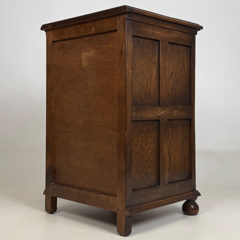 A small dark oak Edwardian chest featuring four drawers with brass drop handles and turned bun feet. View VI