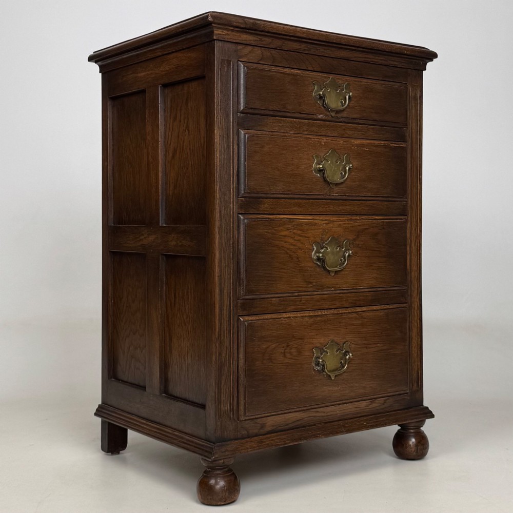 A small dark oak Edwardian chest featuring four drawers with brass drop handles and turned bun feet. View VIII