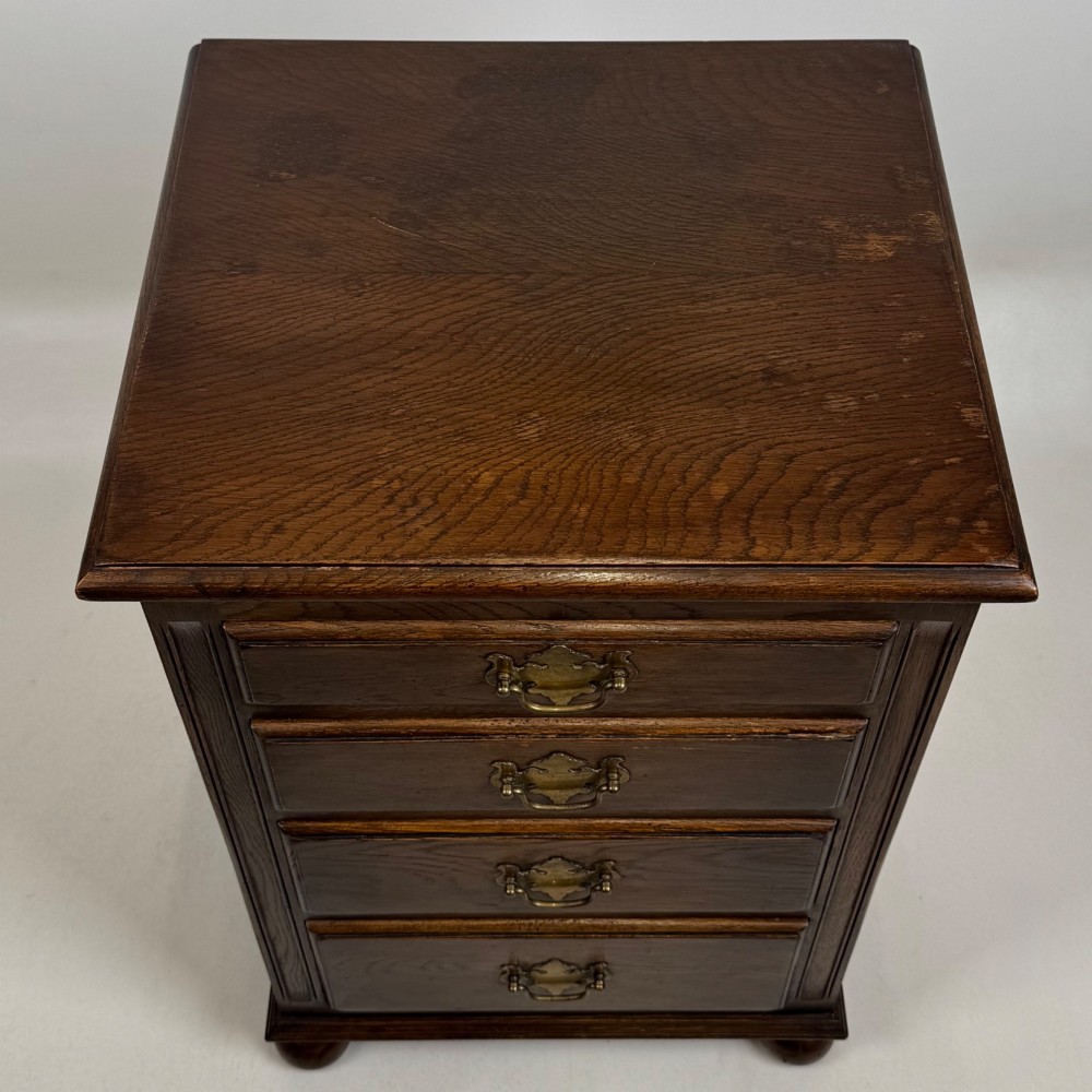A small dark oak Edwardian chest featuring four drawers with brass drop handles and turned bun feet. View XI