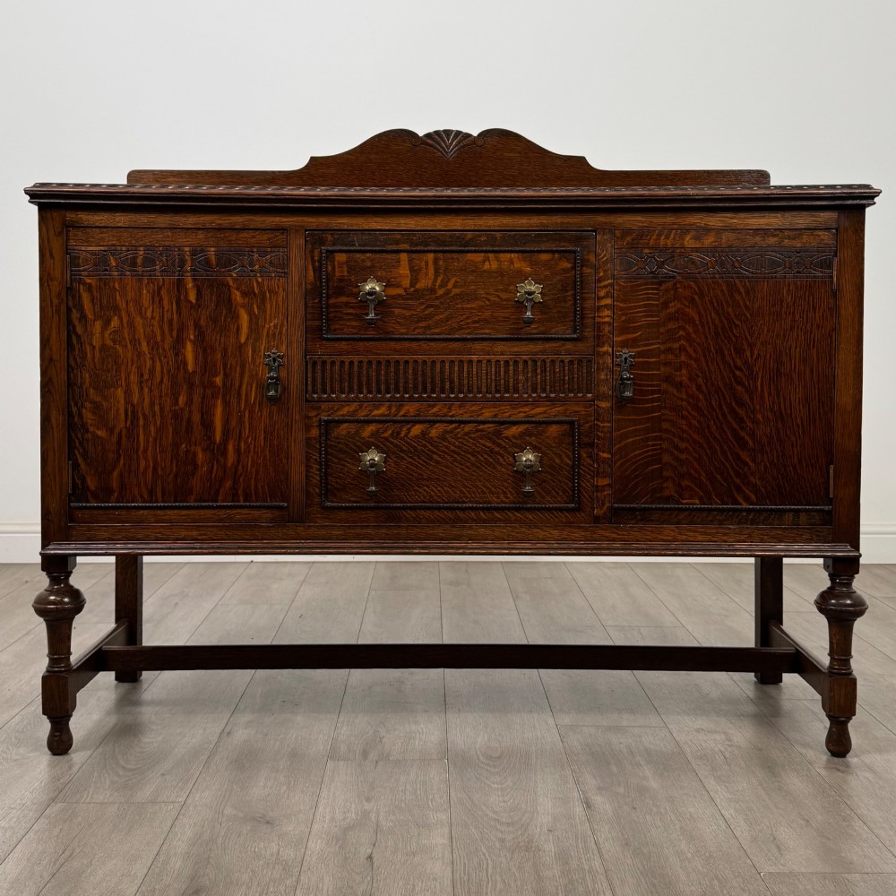 An Edwardian dark oak sideboard featuring two central drawers flanked by cupboard doors, raised on turned front legs with a low back gallery.