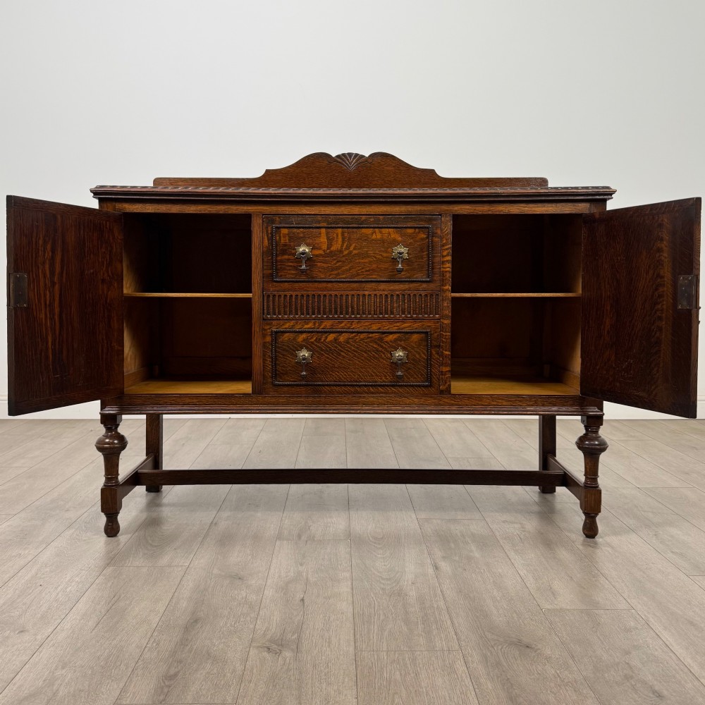 An Edwardian dark oak sideboard featuring two central drawers flanked by cupboard doors, raised on turned front legs with a low back gallery. View II