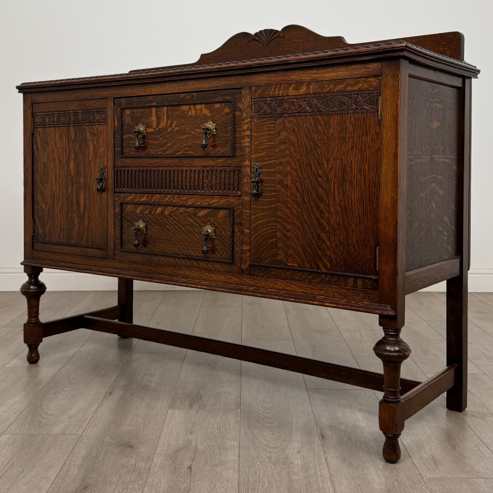 An Edwardian dark oak sideboard featuring two central drawers flanked by cupboard doors, raised on turned front legs with a low back gallery. View III