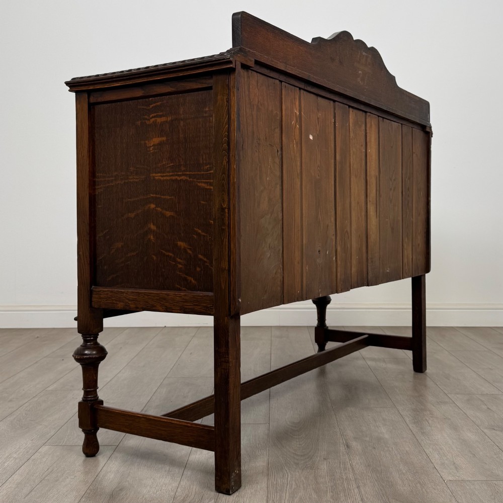 An Edwardian dark oak sideboard featuring two central drawers flanked by cupboard doors, raised on turned front legs with a low back gallery. View IV