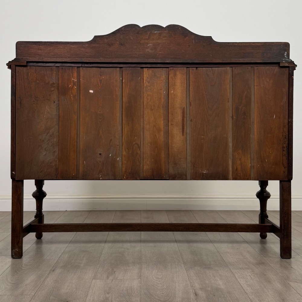 An Edwardian dark oak sideboard featuring two central drawers flanked by cupboard doors, raised on turned front legs with a low back gallery. View V