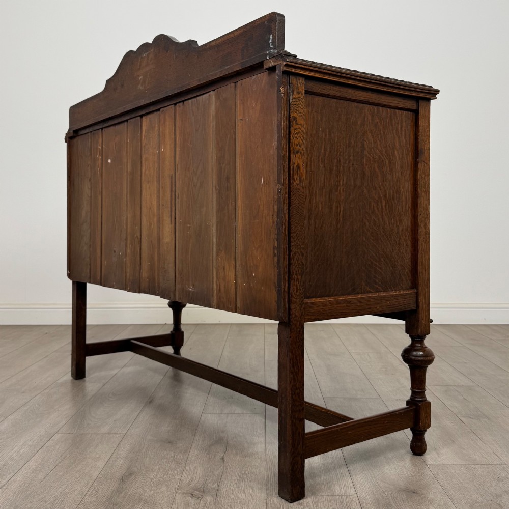 An Edwardian dark oak sideboard featuring two central drawers flanked by cupboard doors, raised on turned front legs with a low back gallery. View VI