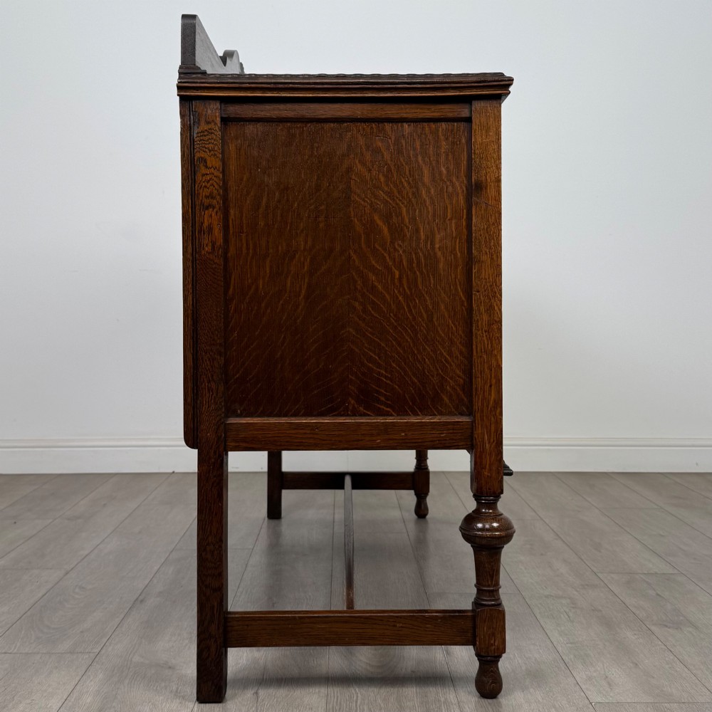 An Edwardian dark oak sideboard featuring two central drawers flanked by cupboard doors, raised on turned front legs with a low back gallery. View VII