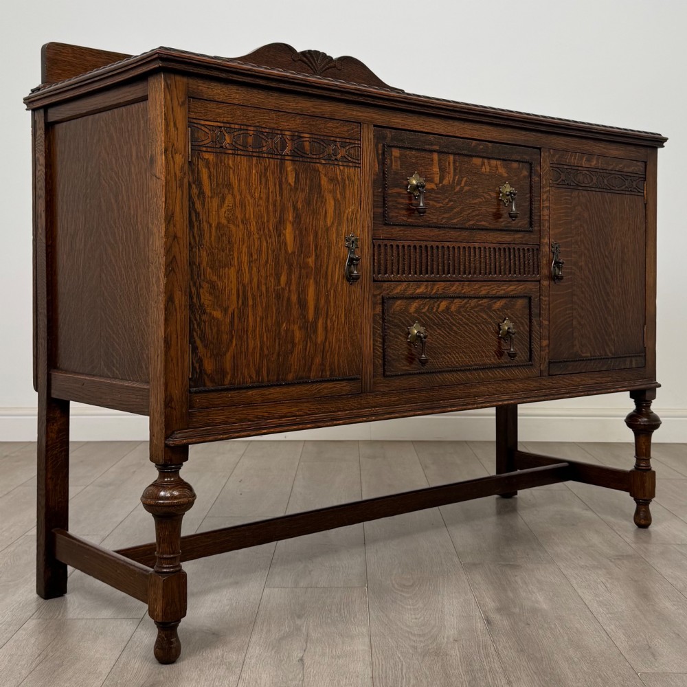 An Edwardian dark oak sideboard featuring two central drawers flanked by cupboard doors, raised on turned front legs with a low back gallery. View VIII