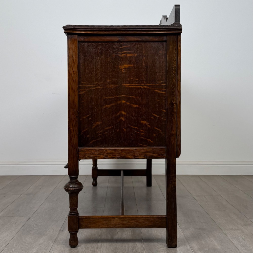 An Edwardian dark oak sideboard featuring two central drawers flanked by cupboard doors, raised on turned front legs with a low back gallery. View IX