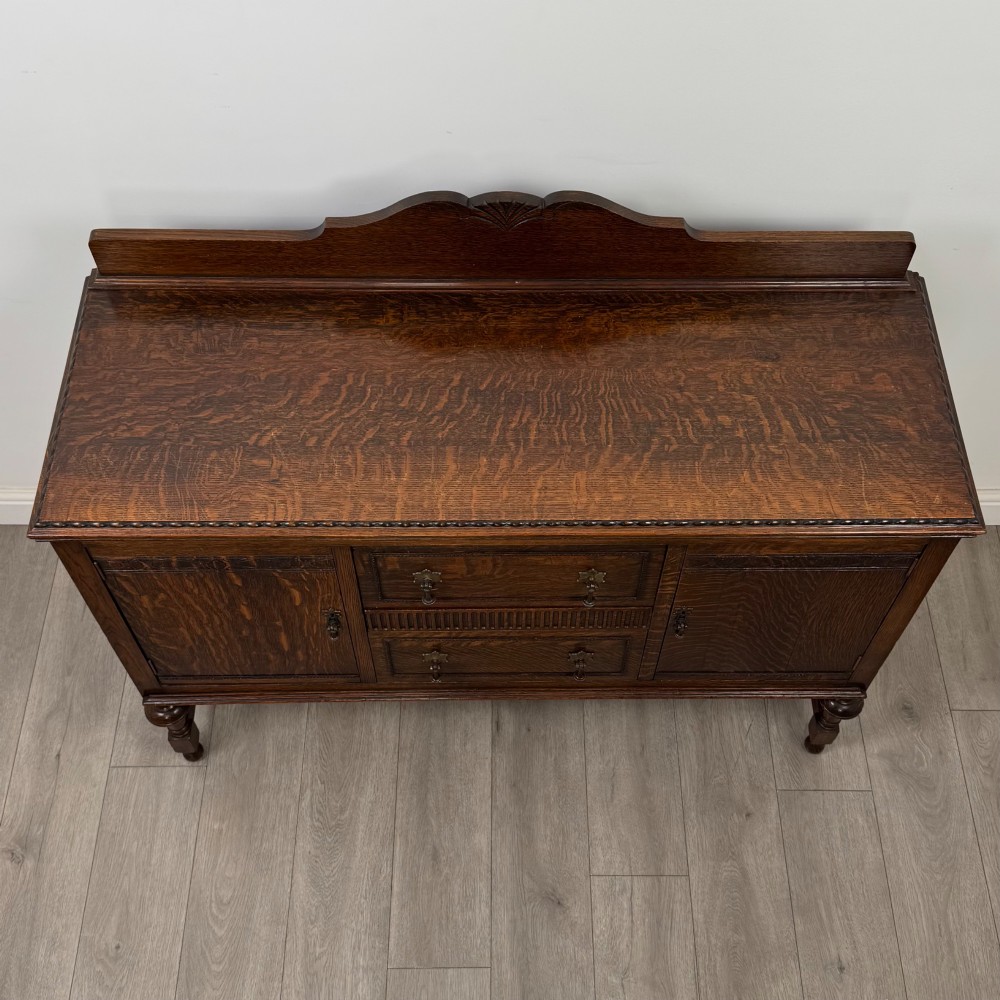An Edwardian dark oak sideboard featuring two central drawers flanked by cupboard doors, raised on turned front legs with a low back gallery. View X