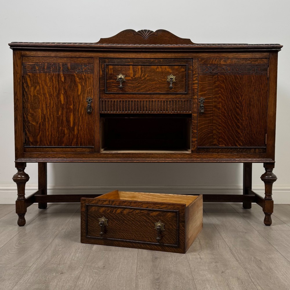 An Edwardian dark oak sideboard featuring two central drawers flanked by cupboard doors, raised on turned front legs with a low back gallery. View XI