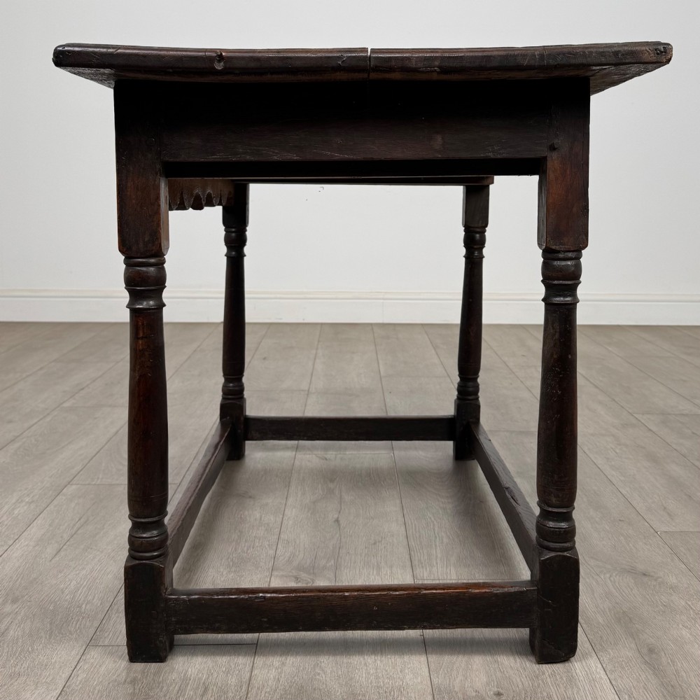 An 18th-century dark oak side table featuring turned legs, a scalloped apron frieze, a single drawer with brass hardware, and perimeter stretchers. View III