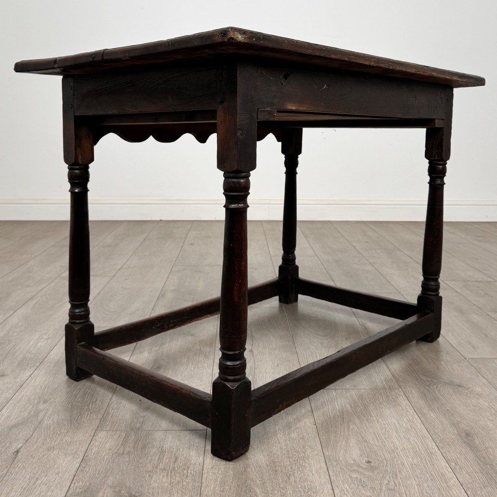 An 18th-century dark oak side table featuring turned legs, a scalloped apron frieze, a single drawer with brass hardware, and perimeter stretchers. View IV