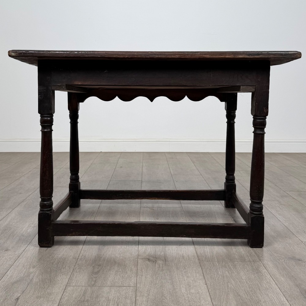 An 18th-century dark oak side table featuring turned legs, a scalloped apron frieze, a single drawer with brass hardware, and perimeter stretchers. View V