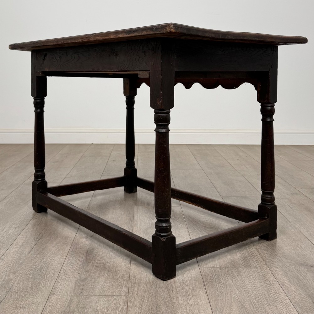 An 18th-century dark oak side table featuring turned legs, a scalloped apron frieze, a single drawer with brass hardware, and perimeter stretchers. View VI