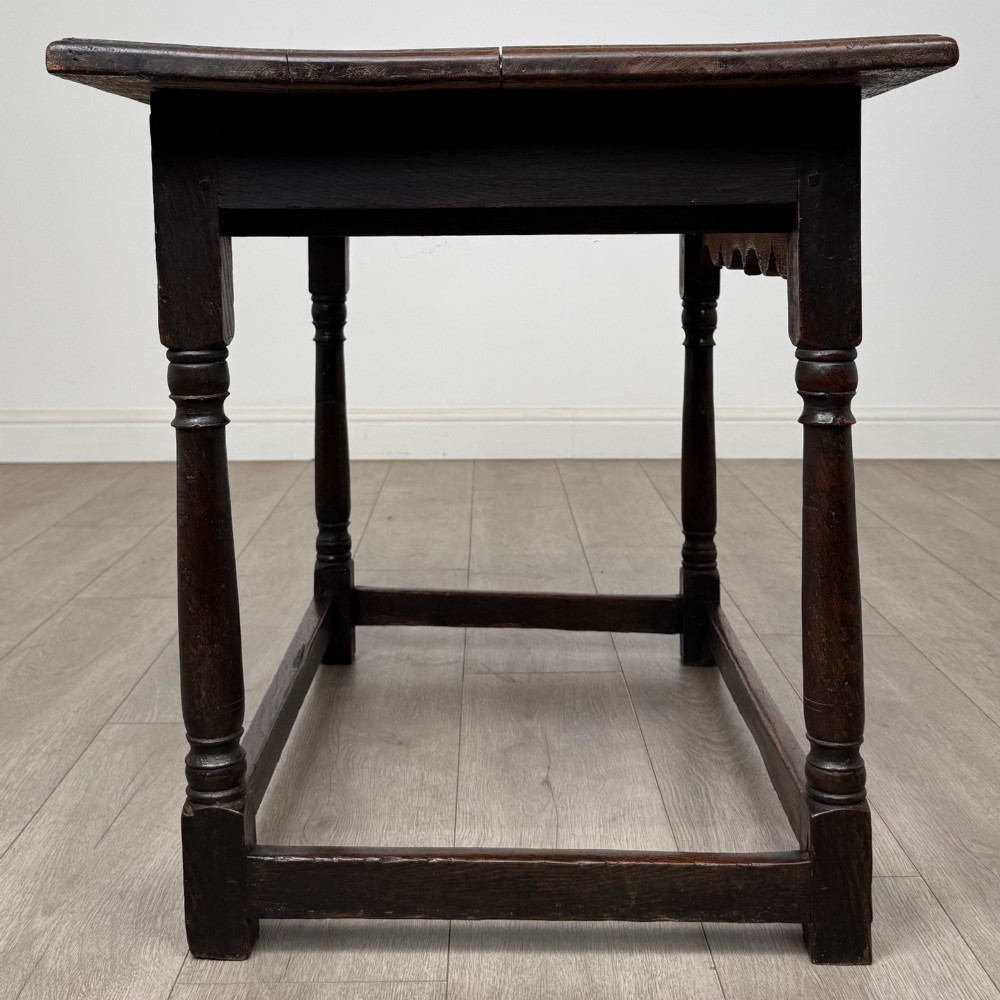An 18th-century dark oak side table featuring turned legs, a scalloped apron frieze, a single drawer with brass hardware, and perimeter stretchers. View VII