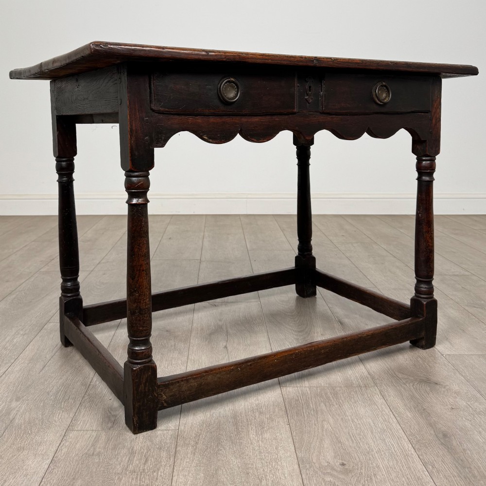 An 18th-century dark oak side table featuring turned legs, a scalloped apron frieze, a single drawer with brass hardware, and perimeter stretchers. View VIII