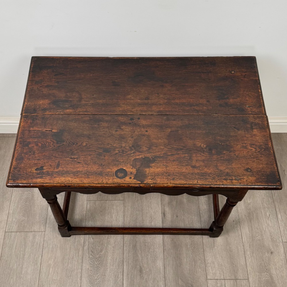 An 18th-century dark oak side table featuring turned legs, a scalloped apron frieze, a single drawer with brass hardware, and perimeter stretchers. View IX