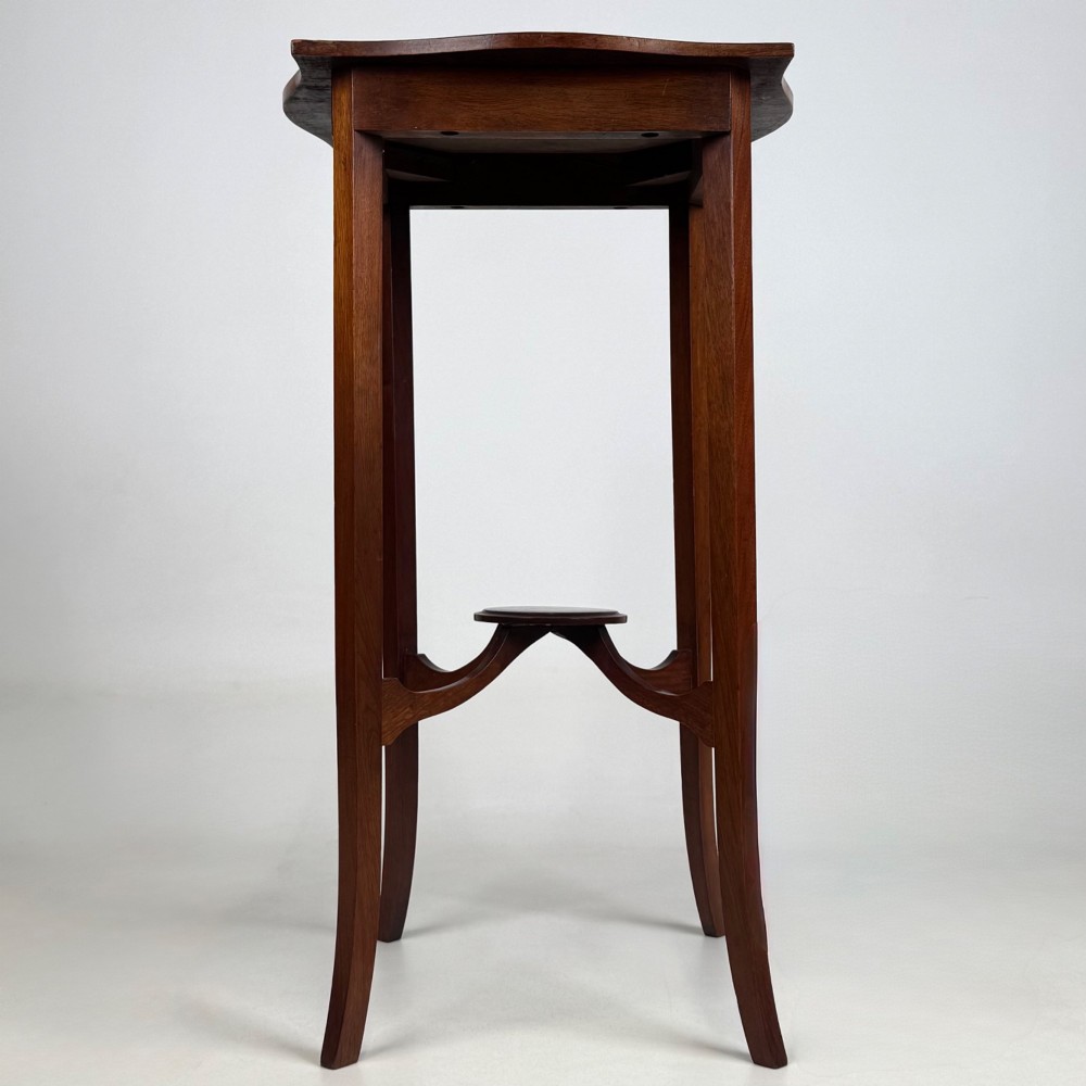 A tall Edwardian mahogany side table featuring a shaped top, slender splayed legs, and an arched stretcher tier.
