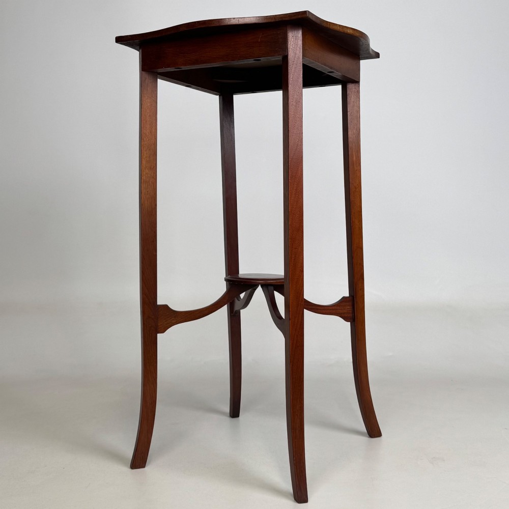 A tall Edwardian mahogany side table featuring a shaped top, slender splayed legs, and an arched stretcher tier. View II