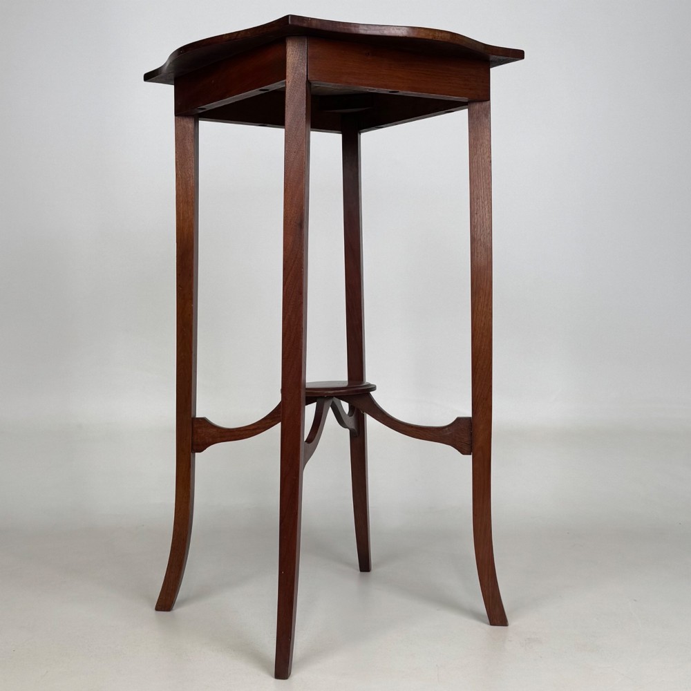 A tall Edwardian mahogany side table featuring a shaped top, slender splayed legs, and an arched stretcher tier. View VI