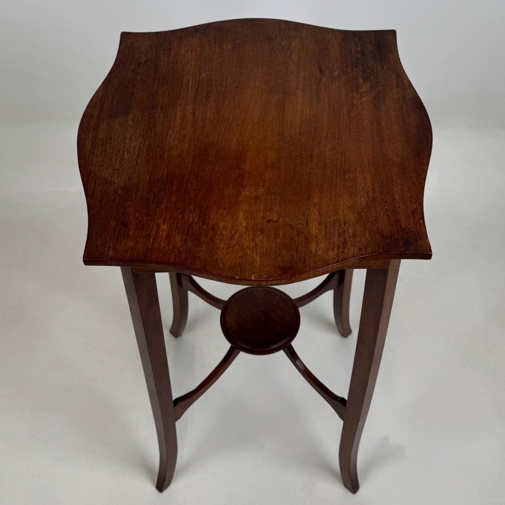 A tall Edwardian mahogany side table featuring a shaped top, slender splayed legs, and an arched stretcher tier. View VII
