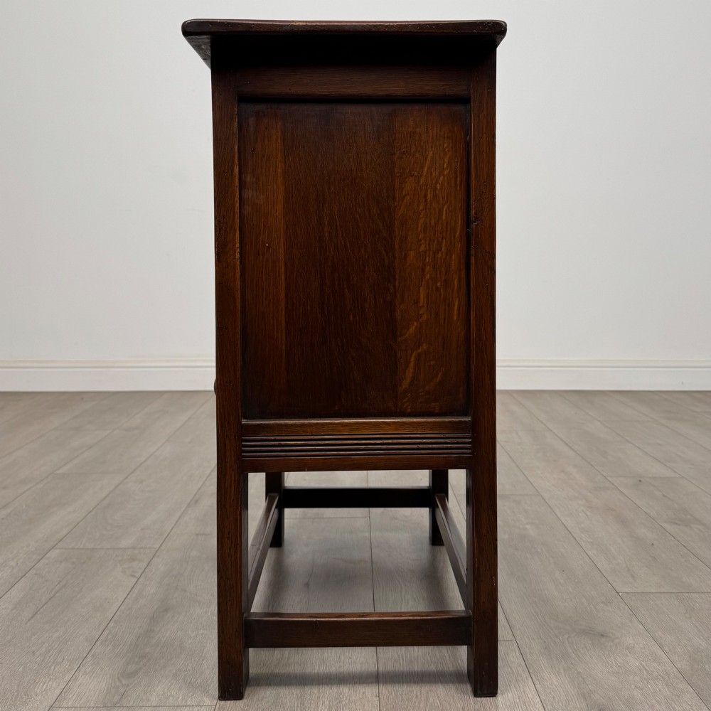 A dark brown carved oak cupboard featuring two arched leaf panel doors, a fluted frieze drawer, and wooden knobs set on squared legs. View IV