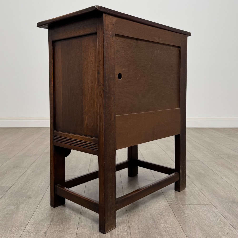 A dark brown carved oak cupboard featuring two arched leaf panel doors, a fluted frieze drawer, and wooden knobs set on squared legs. View V