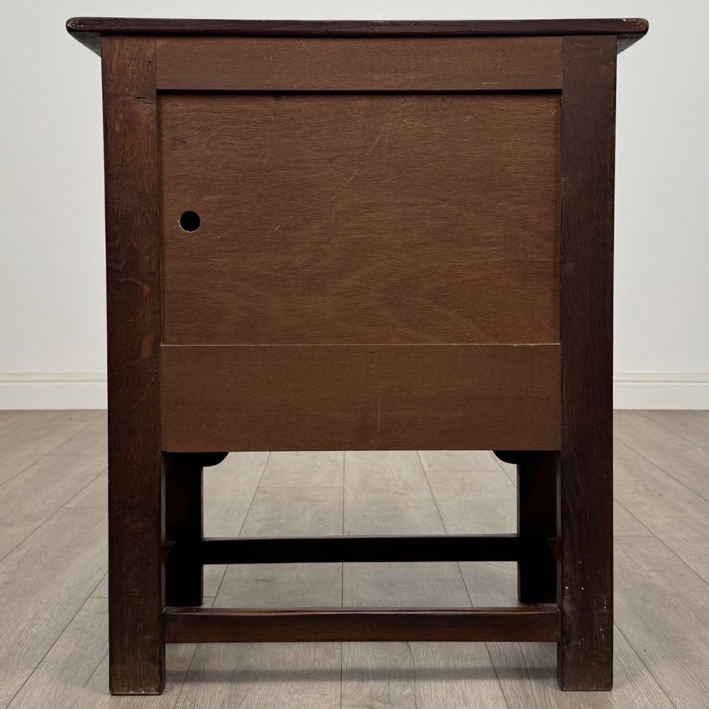 A dark brown carved oak cupboard featuring two arched leaf panel doors, a fluted frieze drawer, and wooden knobs set on squared legs. View VI