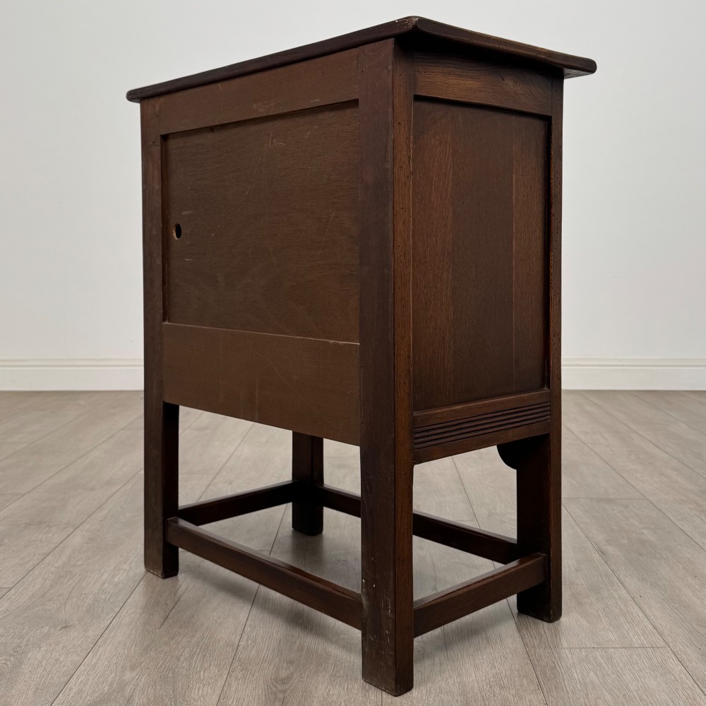 A dark brown carved oak cupboard featuring two arched leaf panel doors, a fluted frieze drawer, and wooden knobs set on squared legs. View VII