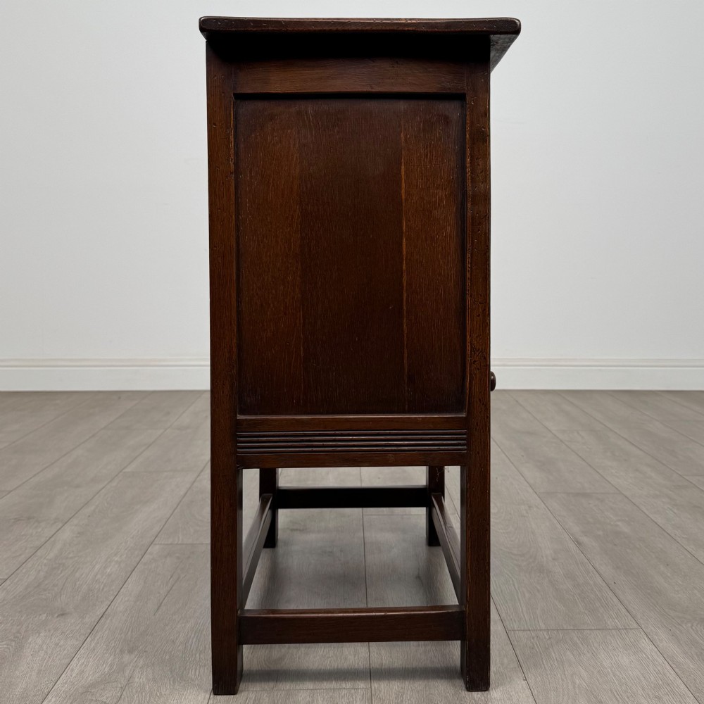 A dark brown carved oak cupboard featuring two arched leaf panel doors, a fluted frieze drawer, and wooden knobs set on squared legs. View VIII