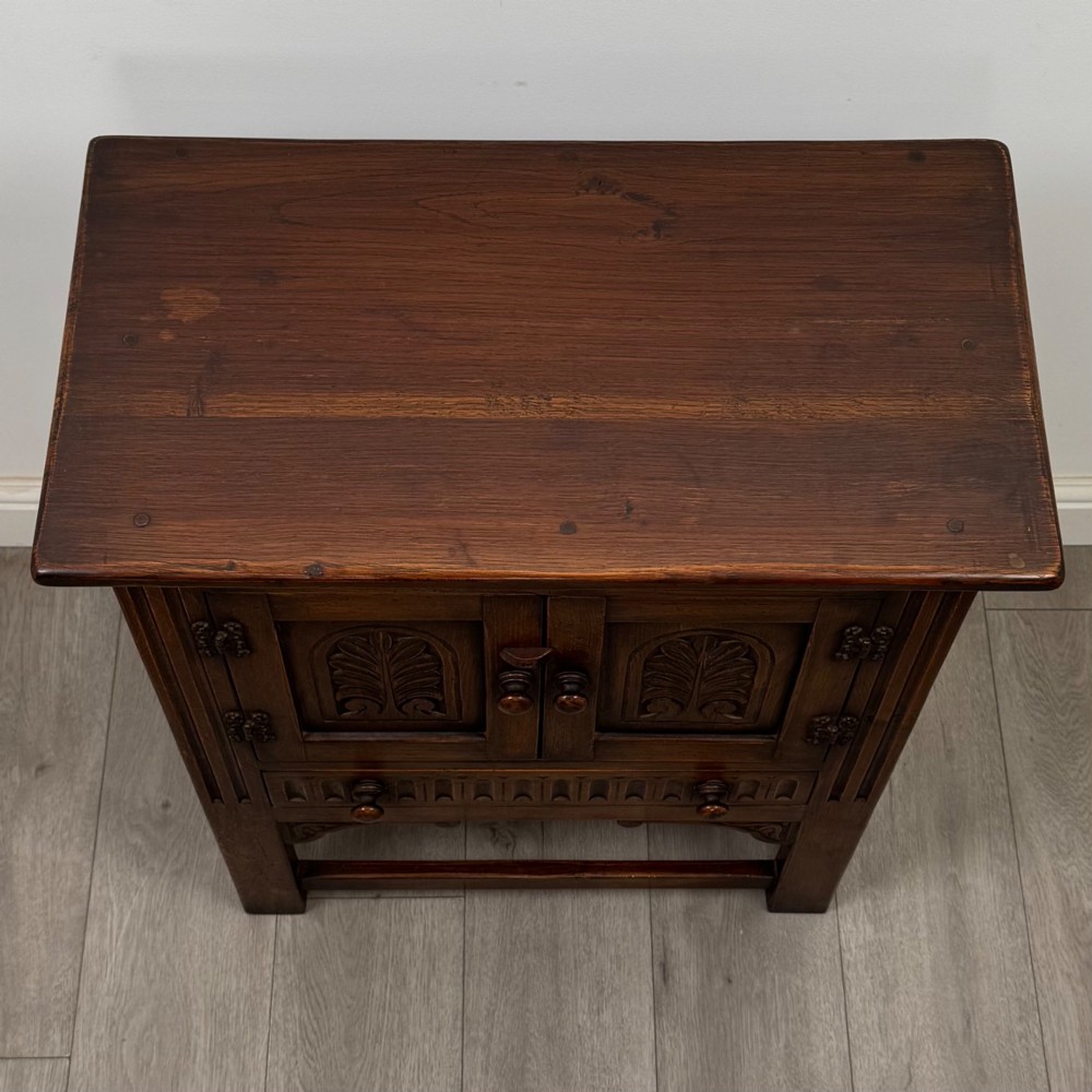 A dark brown carved oak cupboard featuring two arched leaf panel doors, a fluted frieze drawer, and wooden knobs set on squared legs. View X