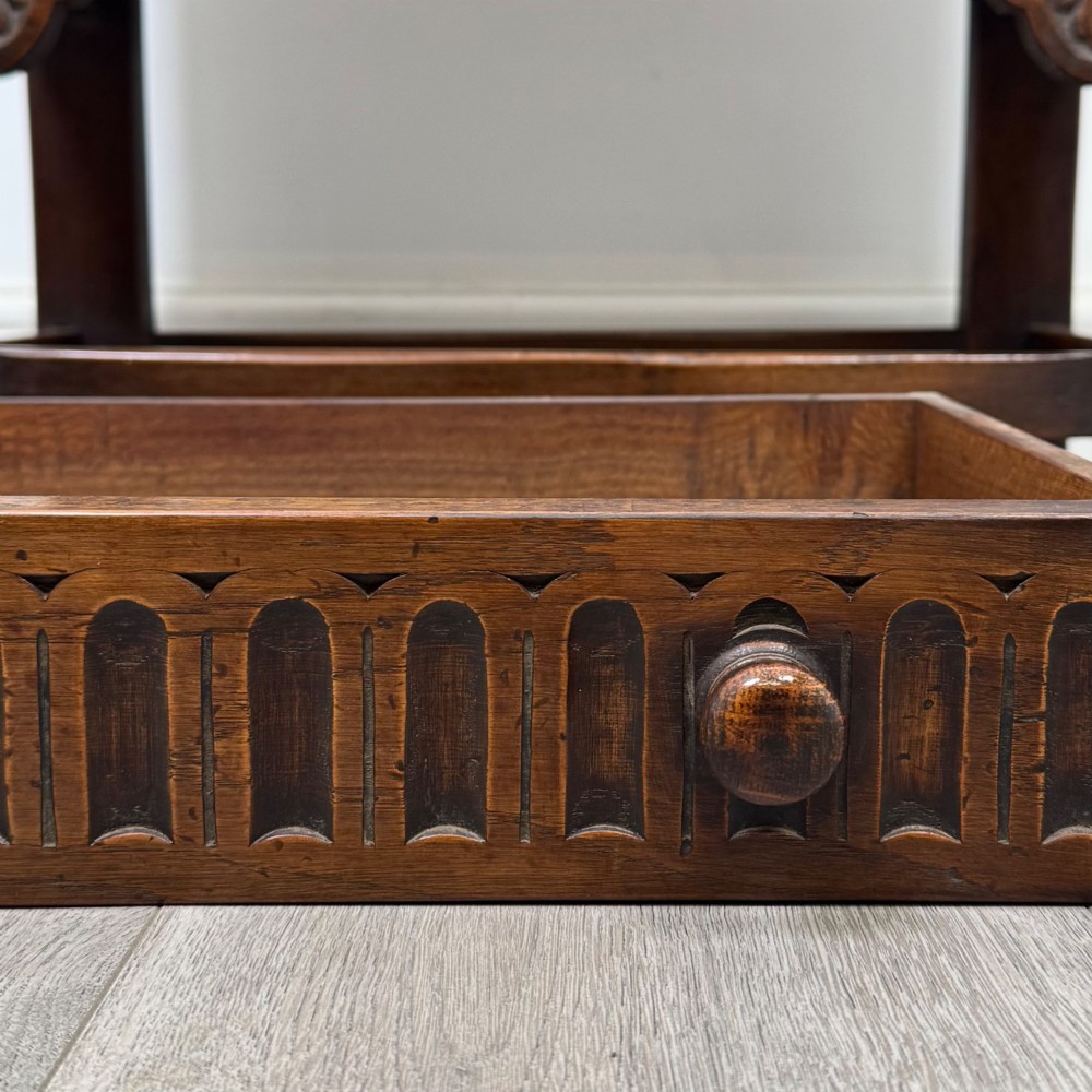 A dark brown carved oak cupboard featuring two arched leaf panel doors, a fluted frieze drawer, and wooden knobs set on squared legs. View XII