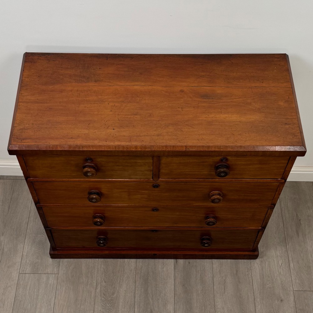 A nineteenth-century Victorian mahogany chest of drawers featuring a two over three drawer layout with turned wooden knobs and a plinth base. View IX