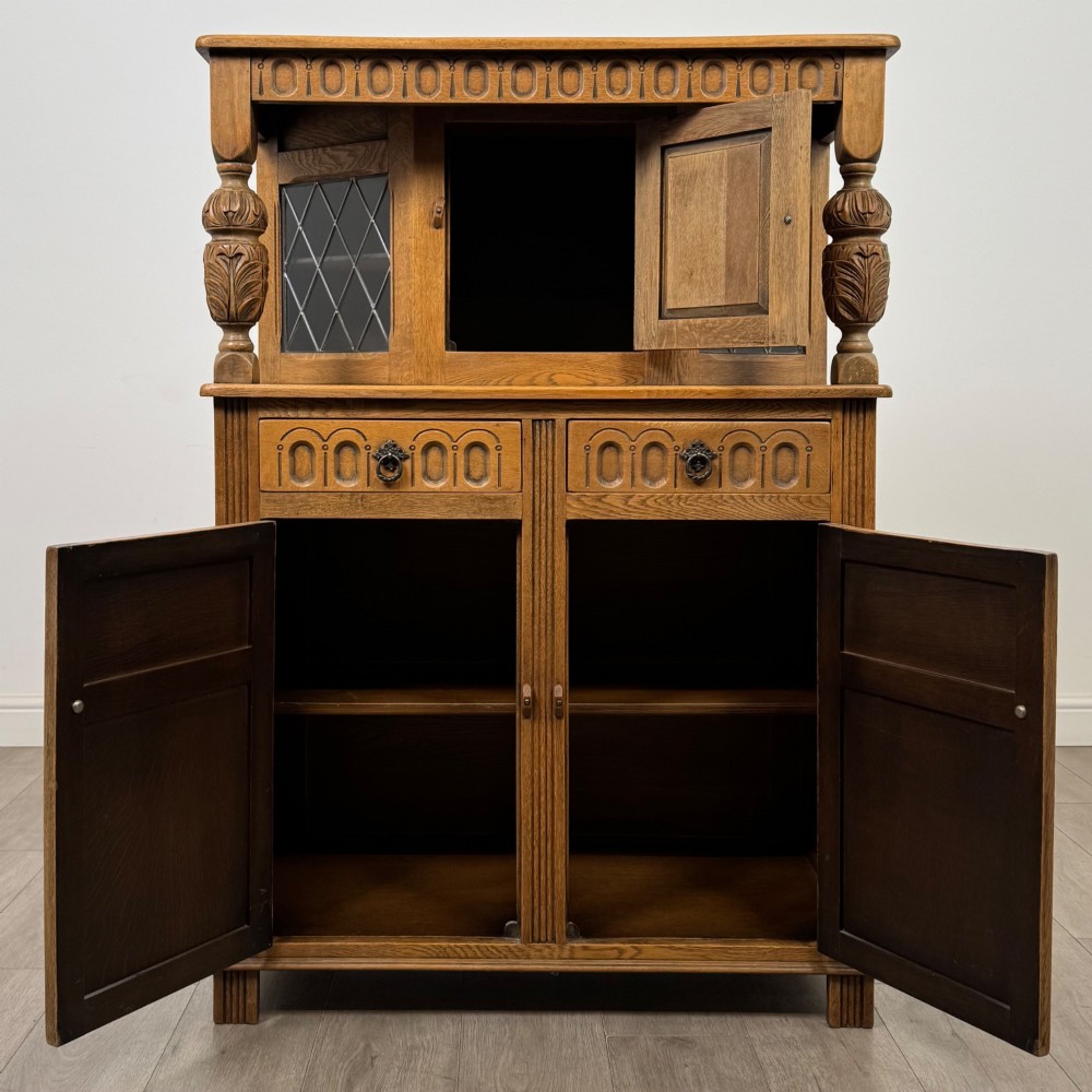 A twentieth-century golden oak court cupboard featuring carved panels, leaded glass side doors, and turned bulbous supports. View II