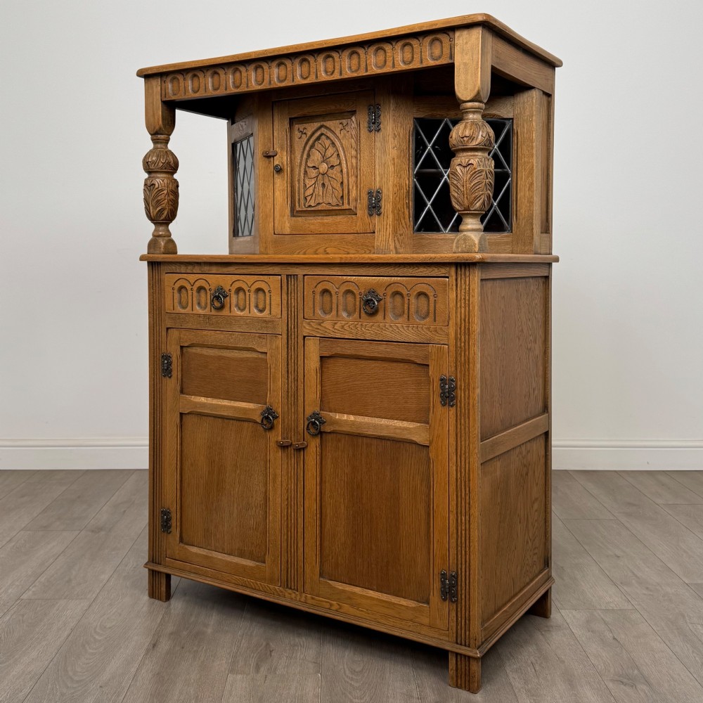 A twentieth-century golden oak court cupboard featuring carved panels, leaded glass side doors, and turned bulbous supports. View III
