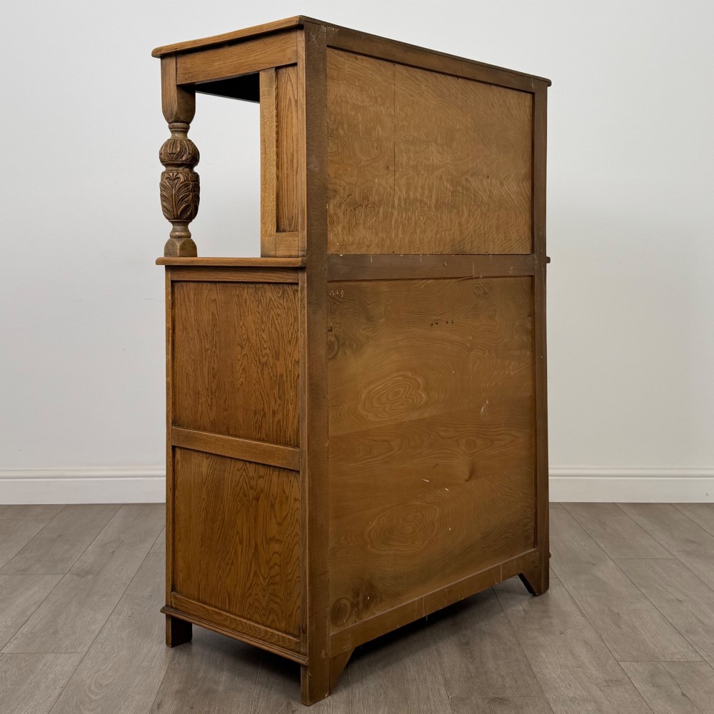 A twentieth-century golden oak court cupboard featuring carved panels, leaded glass side doors, and turned bulbous supports. View V