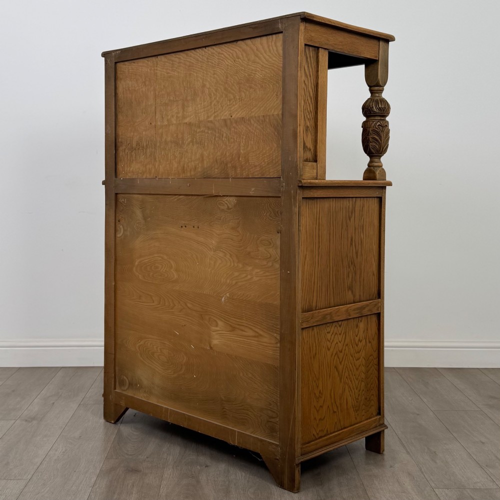 A twentieth-century golden oak court cupboard featuring carved panels, leaded glass side doors, and turned bulbous supports. View VII