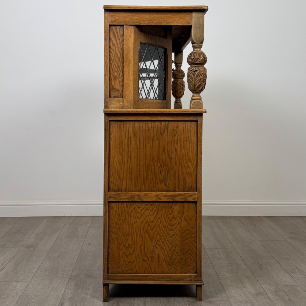 A twentieth-century golden oak court cupboard featuring carved panels, leaded glass side doors, and turned bulbous supports. View VIII
