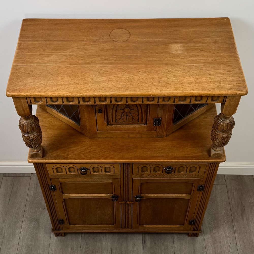 A twentieth-century golden oak court cupboard featuring carved panels, leaded glass side doors, and turned bulbous supports. View X